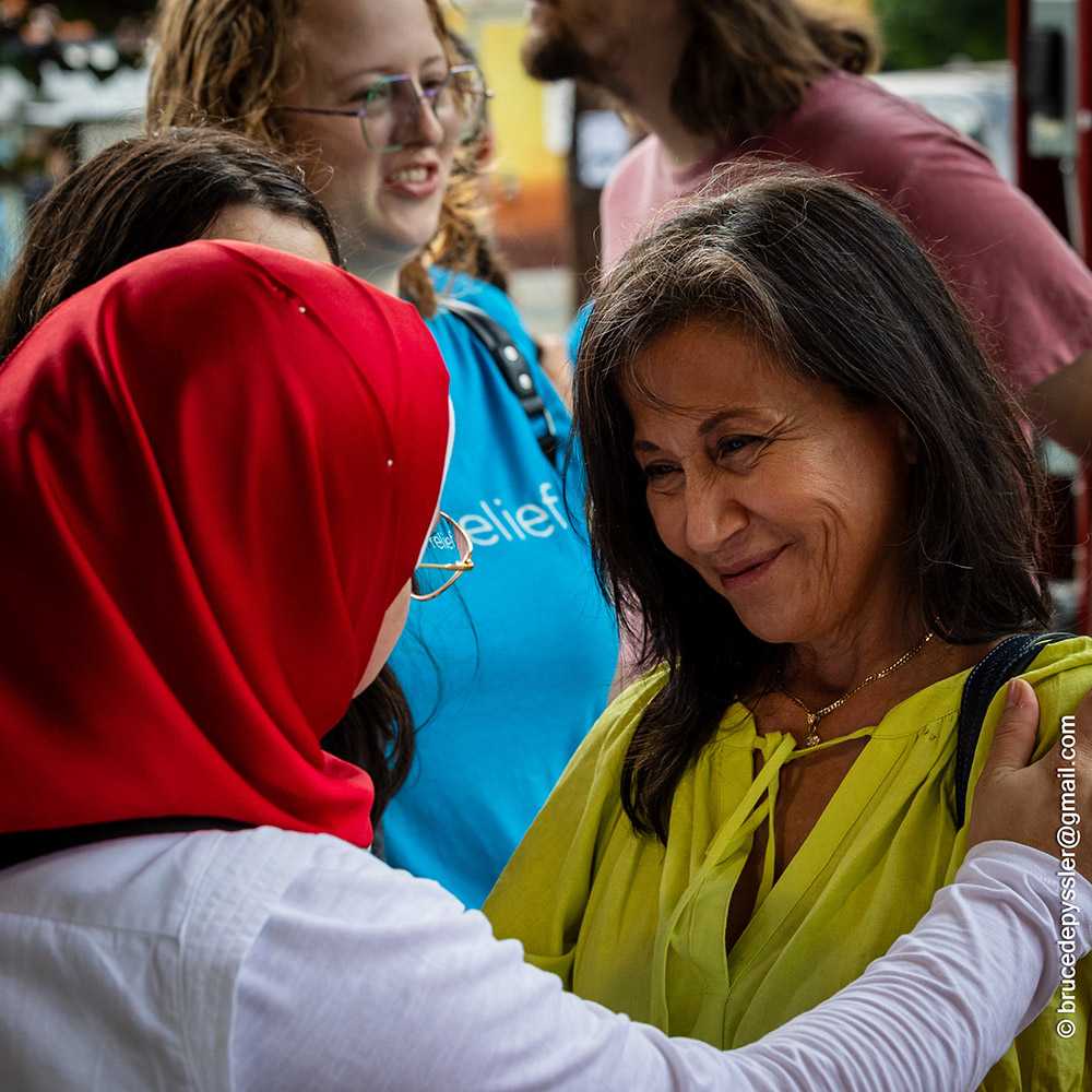 Two women smiling and greeting each other at an outdoor community event